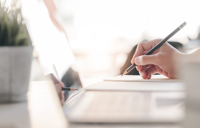 Closeup view of man hand writing on notebook with pencil. Side view.